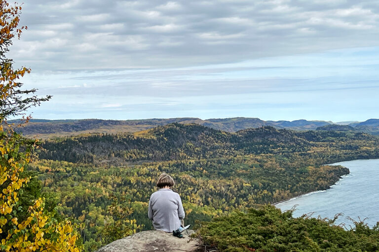 Image of person sitting at the top of Mount Josephine and looking over lake superior