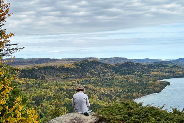 Image of person sitting at the top of Mount Josephine and looking over lake superior